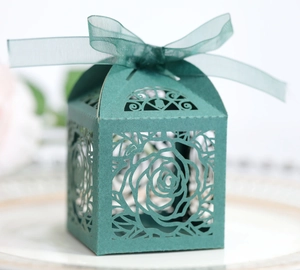 Detail of dark green laser-cut wedding favor box with rose patterns and silk ribbon bow