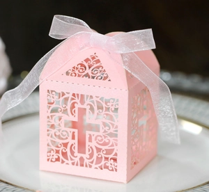 Detail of pink laser-cut cross gift box with white ribbon bow on white ceramic plate