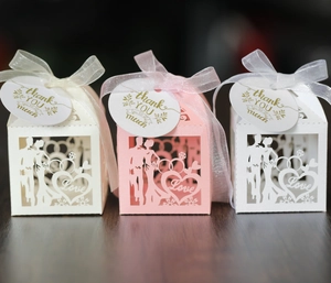 Detail of laser-cut wedding favor boxes with bride and groom silhouettes and ribbon