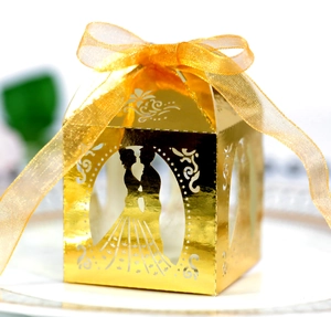 Close-up of laser-cut gold wedding favor box with ribbon bow and hollow silhouette