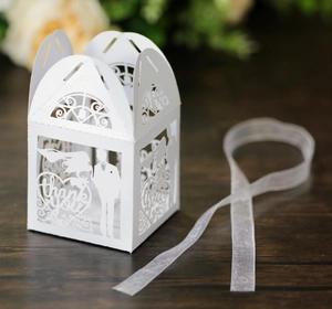 Detail of laser-cut white wedding favor box with bride groom silhouettes and ribbon