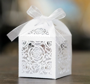 Macro detail of laser-cut white favor box with elegant rose patterns and ribbon bow
