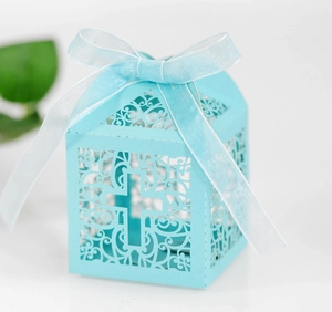 Close-up of light blue laser-cut cross favor box with delicate hollow floral patterns and ribbon
