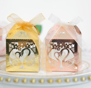 Detail of laser-cut swan heart candy boxes in gold and rose gold with organza ribbons