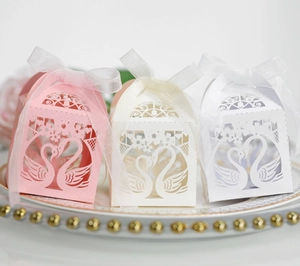 Detail of laser-cut swan gift boxes with delicate ribbons on a decorative plate