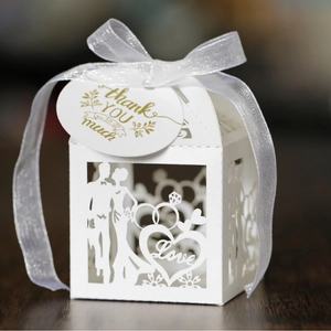 White laser-cut wedding favor box with heart patterns and gold thank you tag with ribbon