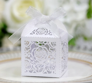Detail of white laser-cut rose hollow favor box with elegant organza ribbon on ceramic plate