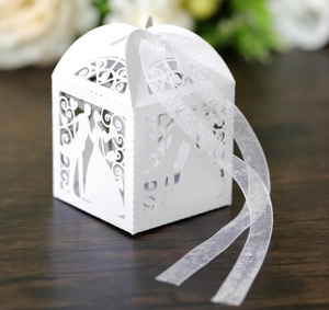 Detail of laser-cut wedding favor box with bride and groom silhouette and white ribbon