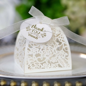 Detailed view of white laser-cut favor box with ribbon and gold Thank You tag on a plate