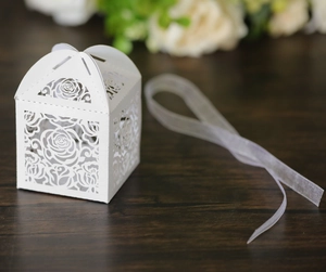 Detail of white laser-cut rose hollow candy box with elegant organza ribbon on wood
