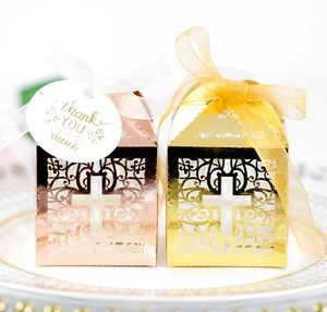Detail of laser cut cross favor boxes in shiny rose gold and gold with ribbon