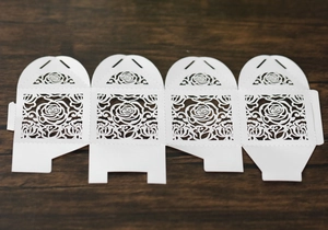 Detailed laser-cut rose patterns on white paper wedding favor box template flat lay