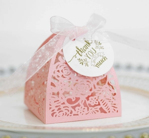 Close-up of pink laser-cut wedding favor box with ribbon and thank you tag on a gold-rimmed plate