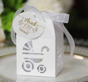 Macro shot of white laser-cut baby stroller candy box with ribbon and gold thank you tag