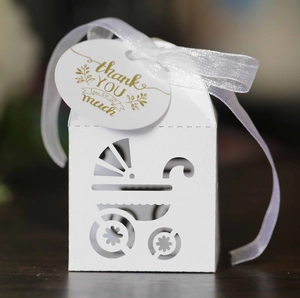 Close-up of white laser-cut baby carriage gift box with silk ribbon and thank you tag