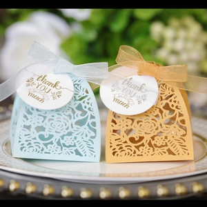 Detail of laser-cut wedding favor boxes in blue and gold with silk ribbons and tags