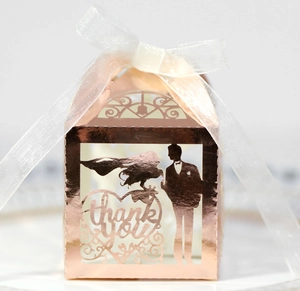 Vue détaillée d'une boîte à dragées or rose ajourée avec silhouette de mariés et ruban