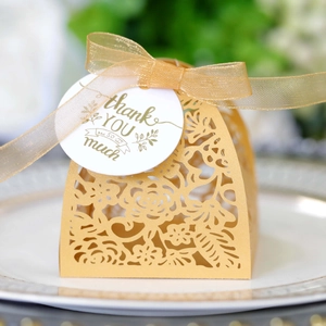 Detail of laser-cut gold gift box with lace pattern and thank you tag on a ceramic plate