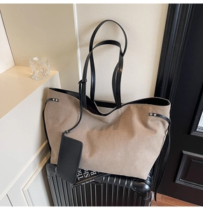 Detail of khaki tote bag with black leather straps and hanging pouch on a black suitcase