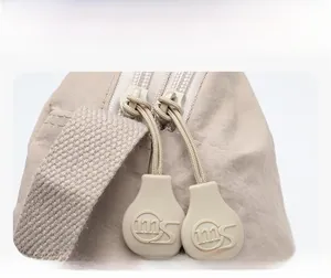 Detailed macro view of the custom double zipper pullers and woven strap on a beige saddle bag