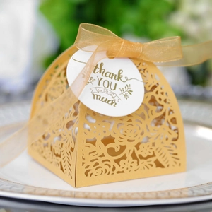 Detail of laser-cut gold wedding favor box with floral patterns and a thank you tag