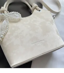 Détail du sac seau crème texturé avec lettrage argenté, perles et breloque en dentelle