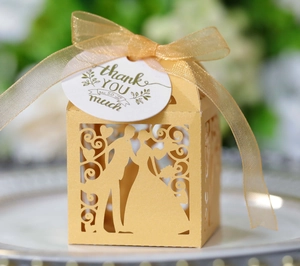 Détail de boîte cadeau de mariage dorée ajourée avec silhouette et ruban en satin