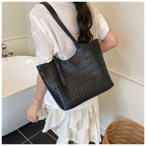 Photo lifestyle d'un grand sac cabas noir ajouré au laser avec bandoulière porté par un mannequin