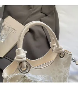 Gros plan sur le sac seau blanc crème avec breloques en perles et détails de poignée en cuir