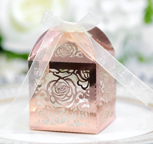 Detail of rose gold laser cut wedding favor box with white ribbon on white ceramic plate