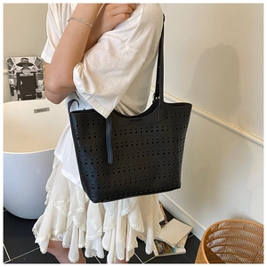 Détail du motif ajouré au laser sur le sac cabas en cuir noir porté à l'épaule par le mannequin