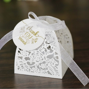 Elegant laser-cut white wedding favor box with a floral pattern, ribbon, and thank you tag