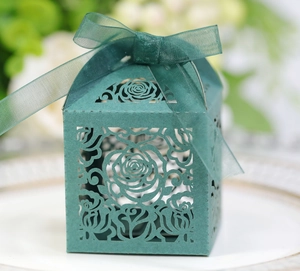 Detail of dark green laser-cut wedding favor box with elegant rose patterns and ribbon