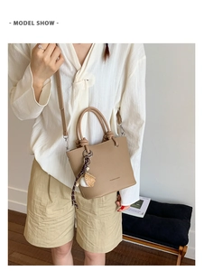 Detail of khaki bucket bag with lychee texture and baseball charm on a shoulder strap