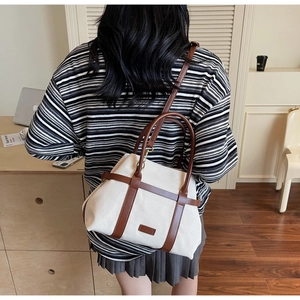 Dettaglio della borsa tote in tela e pelle marrone indossata da una modella in stile casual
