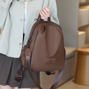 Dettaglio dello zaino in nylon marrone scuro con trama liscia e logo in pelle del brand