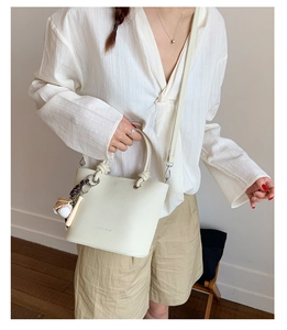 Detail of beige lychee pattern bucket bag with metal rings and baseball charm