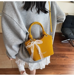 Détail du sac seau jaune en cuir avec nœud en dentelle, breloque perle et logo imprimé