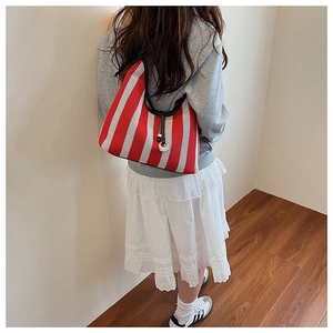 Detail of red and white striped knit tote bag with black trim and charm on shoulder