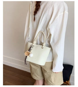 Détail d'un sac seau blanc crème avec texture en cuir grainé et pendentif baseball