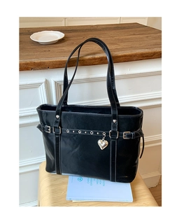 Detail of black glossy tote bag with silver heart charm and metal eyelet straps