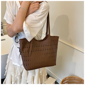 Détail du motif ajouré au laser sur un grand sac cabas en cuir marron avec fines bandoulières