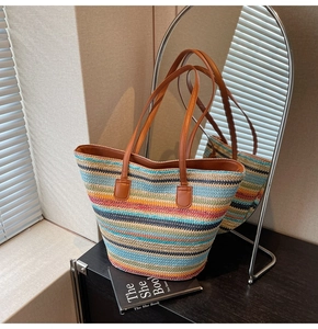 Detail of multi-color woven straw tote bag with brown leather handles in indoor setting