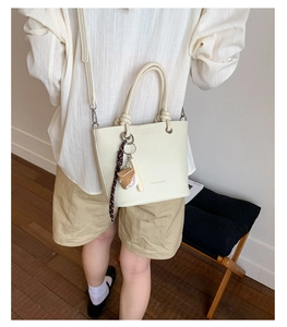 Close-up of beige lychee texture bucket bag with a baseball charm and adjustable strap