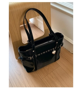 Detail of glossy black patent leather tote bag featuring silver heart charm and buckles