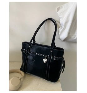 Close-up of glossy black patent leather tote with silver heart pendant and metal buckle detail