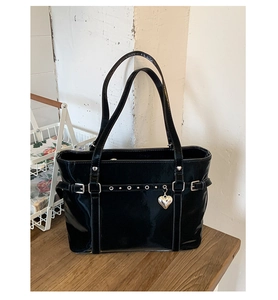 Detail of black glossy patent bucket bag with silver buckles and heart charm on wood