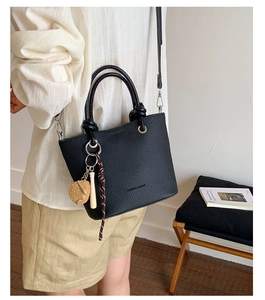 Detail of black litchi grain leather handbag with creative baseball pendant on shoulder strap