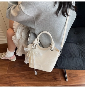 Détail du sac seau crème avec breloque nœud en perles dentelle et poignée nouée