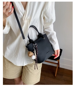 Detail of black lychee leather bucket bag featuring a baseball charm and adjustable strap